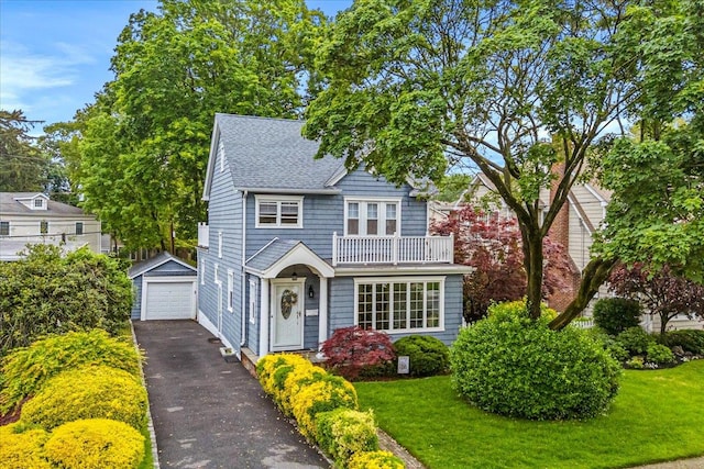 view of front of house with a garage, asphalt driveway, an outdoor structure, roof with shingles, and a front yard