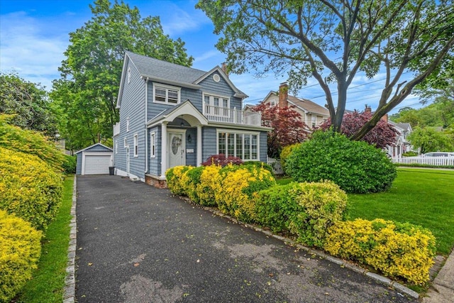 view of front of home with driveway, an outdoor structure, a detached garage, a balcony, and a front yard