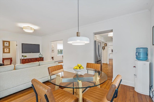dining space featuring wood-type flooring, crown molding, a baseboard heating unit, and baseboards