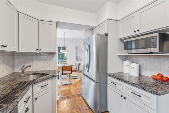 kitchen with appliances with stainless steel finishes, a sink, decorative backsplash, and dark stone counters