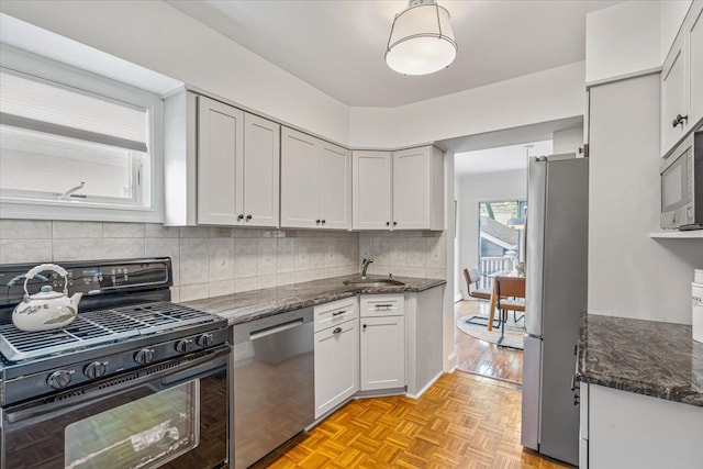 kitchen with stainless steel appliances, dark stone countertops, decorative backsplash, a sink, and white cabinetry