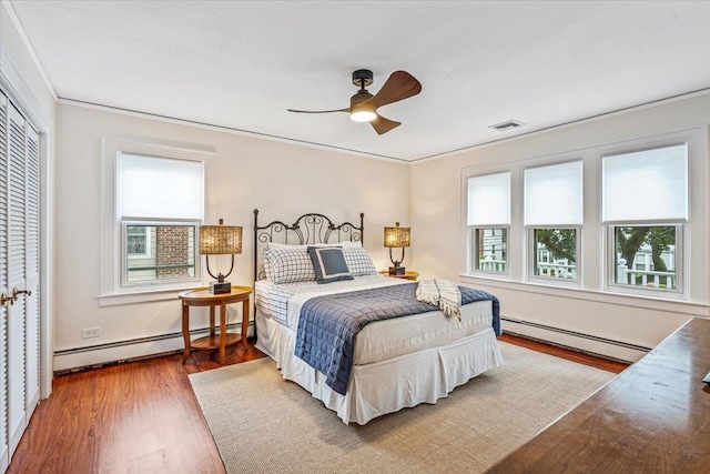 bedroom featuring a baseboard radiator, multiple windows, and wood finished floors