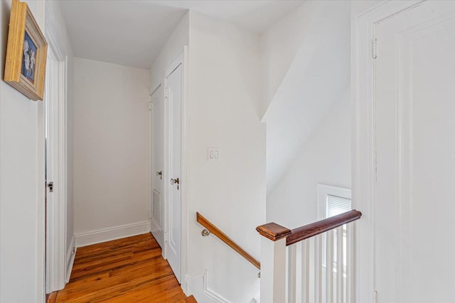 hall with wood finished floors, baseboards, and an upstairs landing
