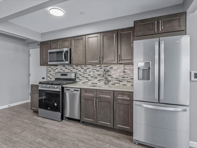 kitchen with stainless steel appliances, a sink, dark brown cabinets, light countertops, and decorative backsplash
