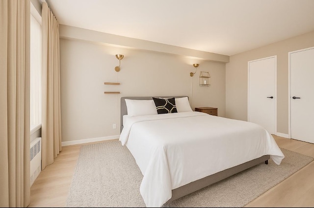 bedroom featuring light wood finished floors, radiator, and baseboards