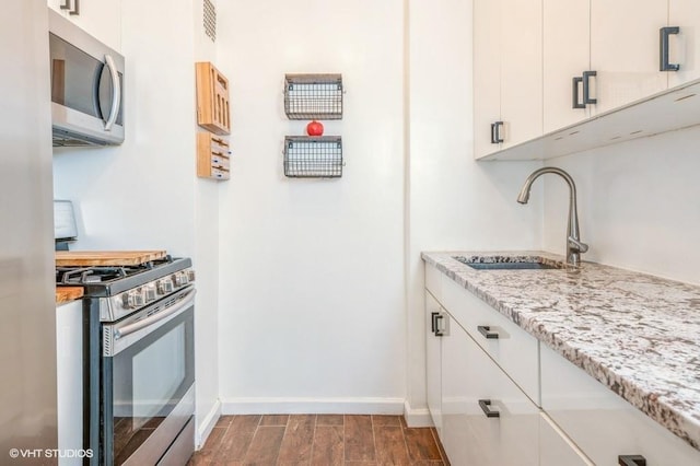 kitchen with appliances with stainless steel finishes, a sink, dark wood finished floors, light stone countertops, and baseboards