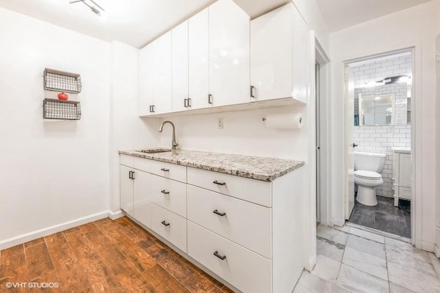 kitchen featuring a sink, white cabinets, light stone countertops, and baseboards