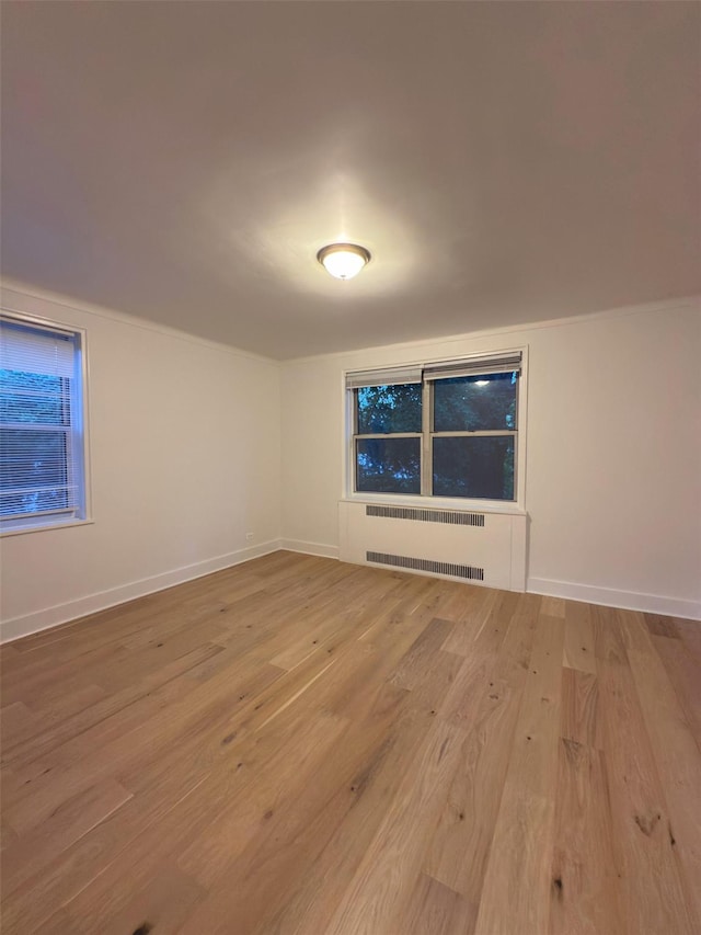 unfurnished room featuring wood finished floors, radiator heating unit, and baseboards
