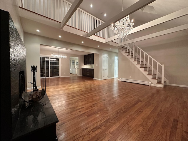107 Norwood Ave, Northport, NY 11768 - unfurnished living room featuring a chandelier, a baseboard radiator, stairs, a towering ceiling, and wood finished floors