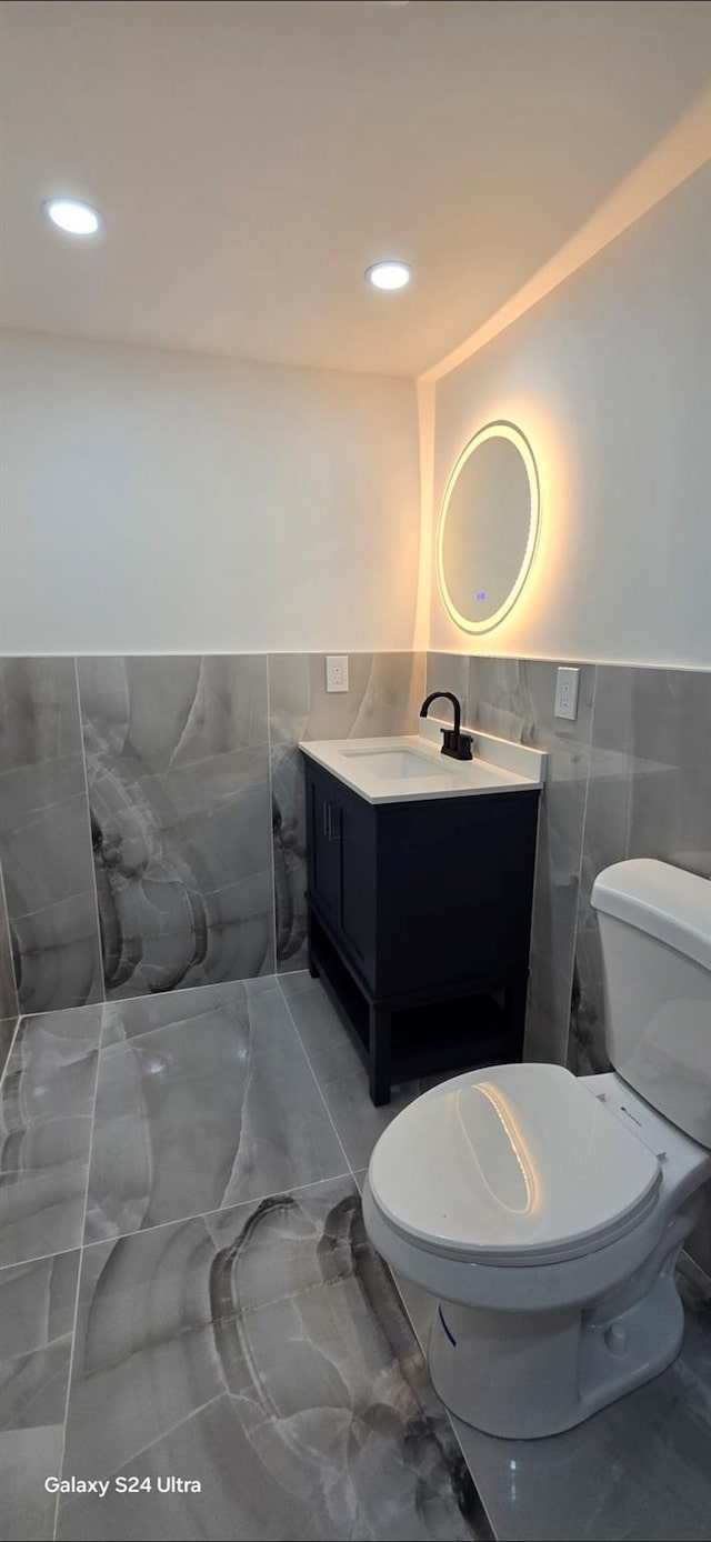 151 Boylston St, Hempstead, NY 11550 - bathroom featuring tile walls, marble look tiles, toilet, vanity, and a wainscoted wall