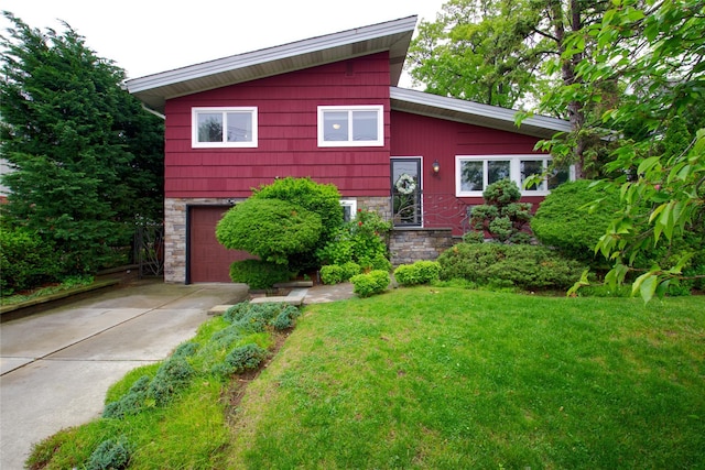 tri-level home with driveway, stone siding, an attached garage, and a front lawn