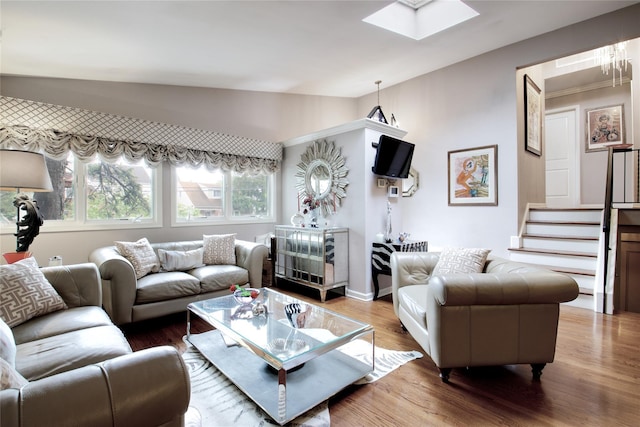 living room featuring lofted ceiling, a skylight, wood finished floors, and stairway
