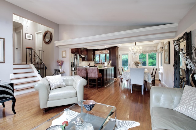 living room with stairs, a chandelier, plenty of natural light, wood finished floors, and vaulted ceiling