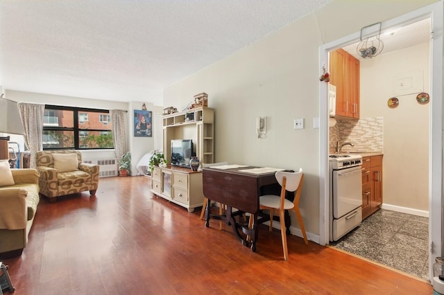 39-60 54th St Unit 3B, Woodside, NY 11377 - living area with radiator, dark wood-style flooring, a desk, a textured ceiling, and baseboards