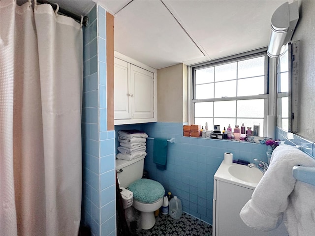 full bathroom featuring toilet, tile walls, tile patterned floors, vanity, and a wainscoted wall