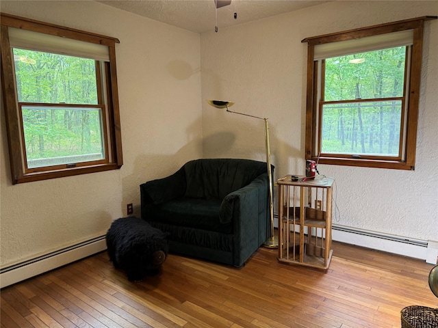 living area featuring a baseboard heating unit, wood-type flooring, a textured wall, and ceiling fan