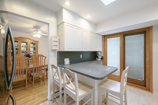 kitchen featuring dark countertops, white cabinetry, a kitchen bar, light wood-style flooring, and stainless steel refrigerator