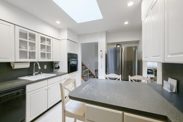 kitchen with black appliances, a sink, dark countertops, decorative backsplash, and white cabinets