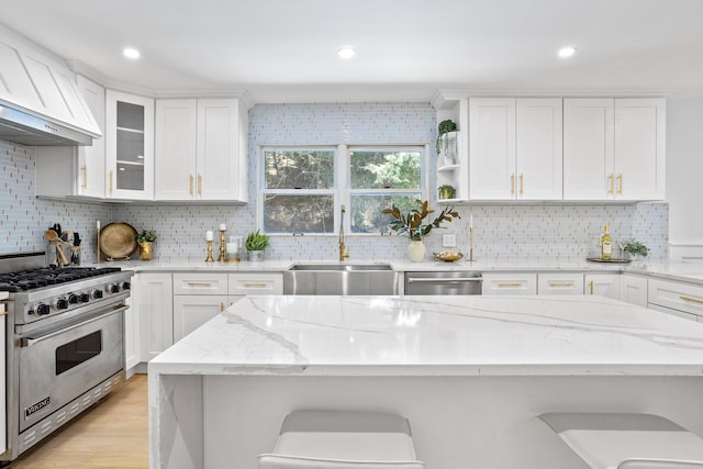 kitchen featuring appliances with stainless steel finishes, a sink, custom range hood, white cabinets, and backsplash