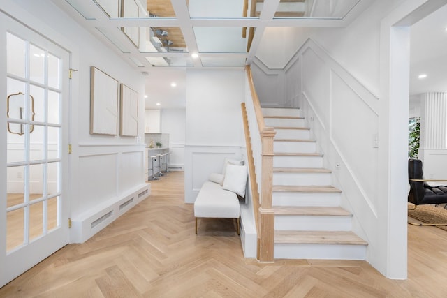 stairway with a decorative wall, a wainscoted wall, recessed lighting, and coffered ceiling