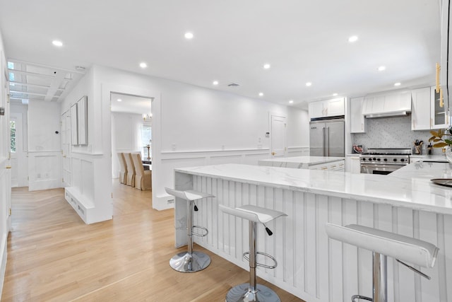 kitchen with high quality appliances, premium range hood, white cabinets, light stone countertops, and light wood finished floors