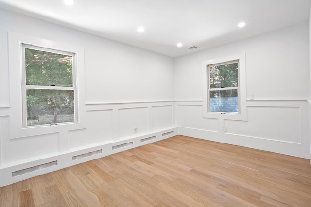 empty room featuring a decorative wall, light wood-type flooring, wainscoting, healthy amount of natural light, and recessed lighting