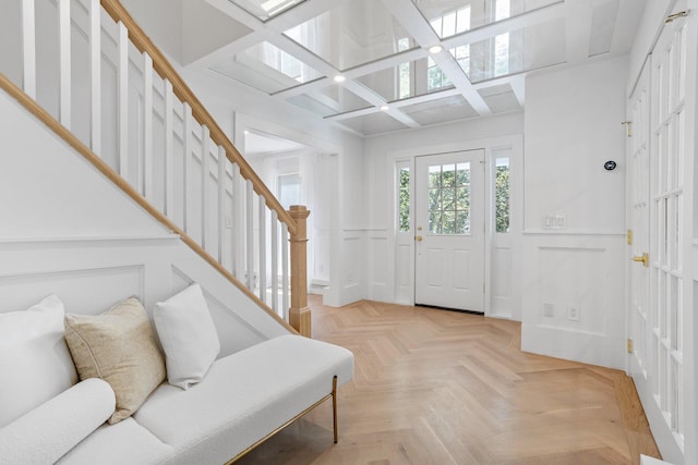 foyer with coffered ceiling, stairway, a decorative wall, wainscoting, and a skylight
