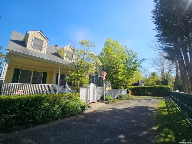 view of side of home featuring fence, covered porch, and asphalt driveway