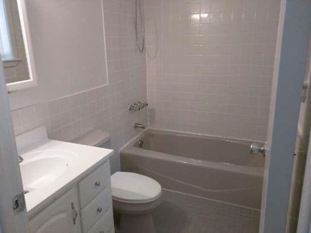bathroom with toilet, tile walls, vanity, and shower / tub combination