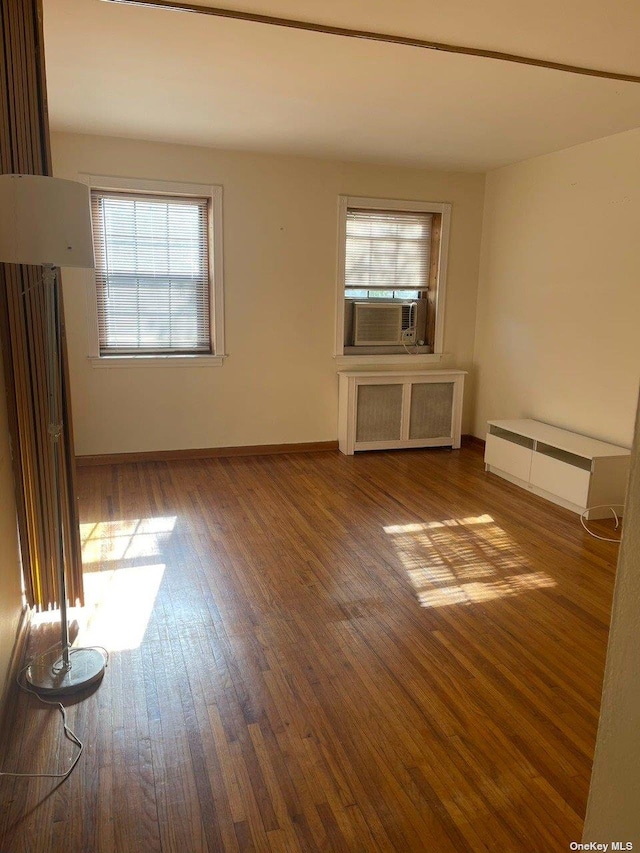 unfurnished living room featuring radiator, cooling unit, wood finished floors, and baseboards