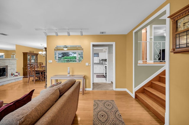living area with light wood finished floors, a fireplace, a chandelier, stairs, and baseboards
