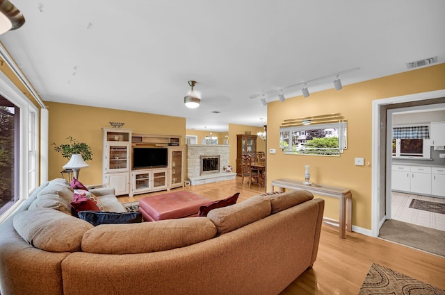 living room with a ceiling fan, a stone fireplace, track lighting, light wood-style floors, and baseboards