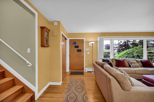 living area featuring baseboards, light wood-style floors, stairs, and a baseboard radiator