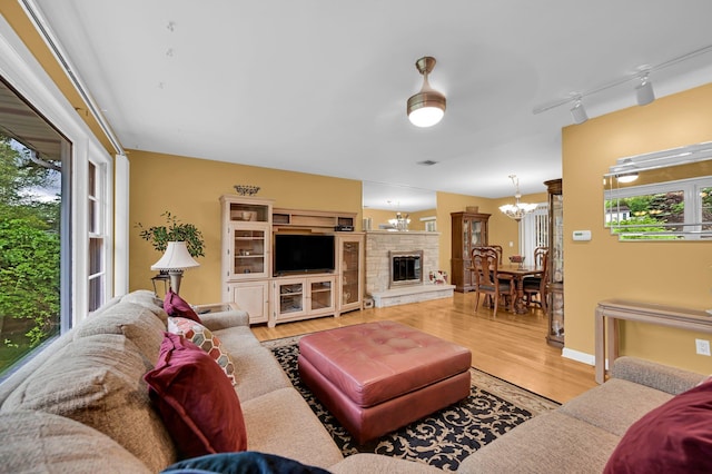 living area with healthy amount of natural light, a chandelier, wood finished floors, and a stone fireplace