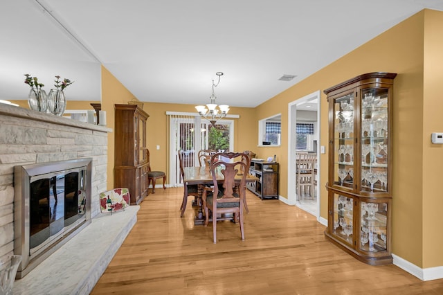 dining room with a chandelier, baseboards, light wood finished floors, and a fireplace