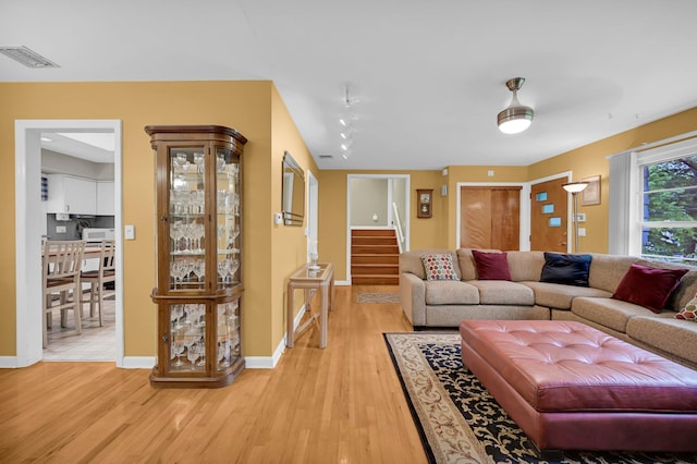 living room featuring light wood-type flooring, stairway, and baseboards