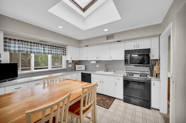 kitchen with black appliances, a sink, light countertops, a skylight, and white cabinets