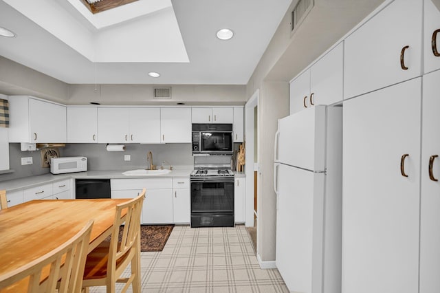 kitchen with black appliances, a sink, a skylight, light countertops, and recessed lighting