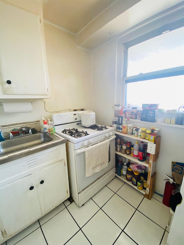 kitchen featuring white gas range oven, white cabinetry, light tile patterned flooring, a sink, and light countertops
