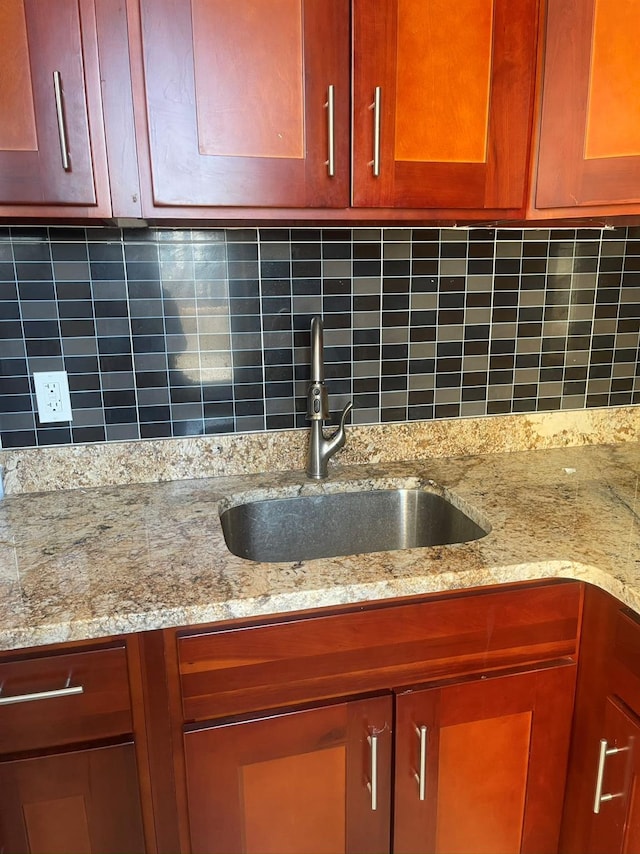 kitchen view of a sink, decorative backsplash, and light stone counters