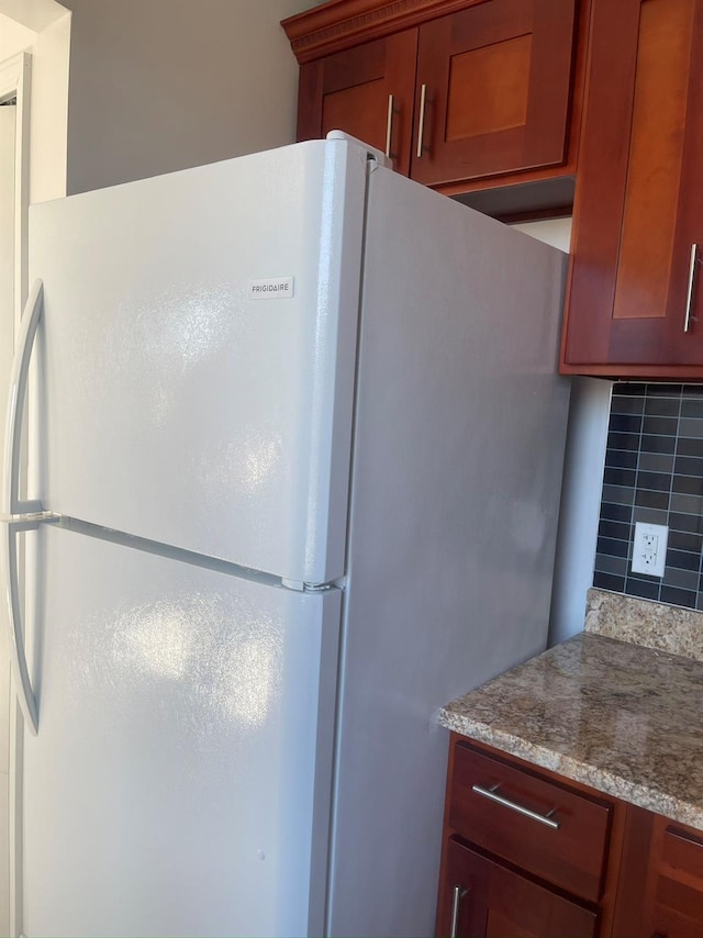 kitchen featuring freestanding refrigerator, tasteful backsplash, light stone counters, and brown cabinetry
