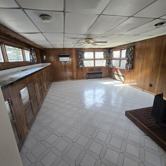 78-10 222nd St, Oakland Gardens, NY 11364 - unfurnished living room featuring wood walls, radiator heating unit, healthy amount of natural light, ceiling fan, and a paneled ceiling