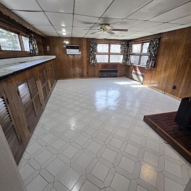78-10 222nd St, Oakland Gardens, NY 11364 - unfurnished living room with wood walls, ceiling fan, a drop ceiling, radiator, and light floors