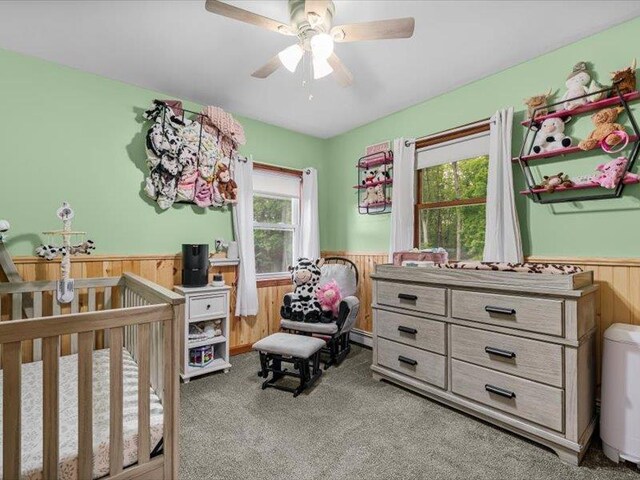 708 Kirbytown Rd, Middletown, NY 10940 - carpeted bedroom with wainscoting, wooden walls, a crib, and ceiling fan