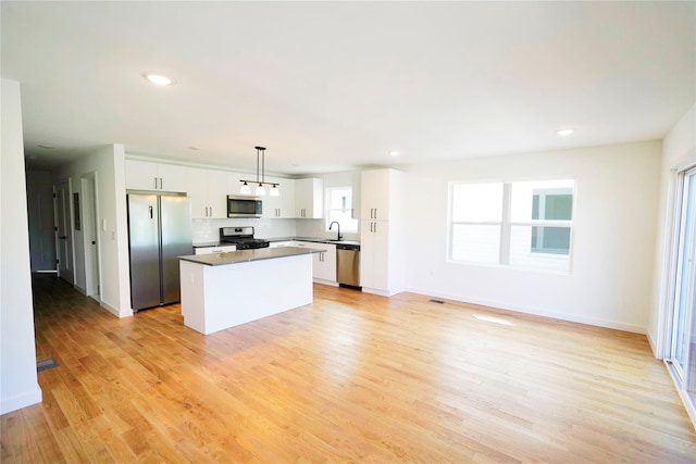 kitchen featuring appliances with stainless steel finishes, a center island, white cabinets, light wood-style flooring, and pendant lighting