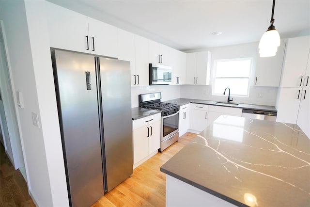 kitchen with appliances with stainless steel finishes, a sink, light wood-style flooring, white cabinets, and pendant lighting