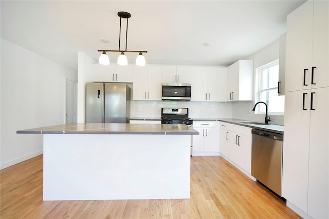 kitchen with appliances with stainless steel finishes, a sink, backsplash, white cabinetry, and light wood finished floors