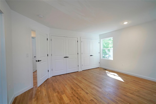 unfurnished bedroom featuring two closets, baseboards, and light wood-style flooring