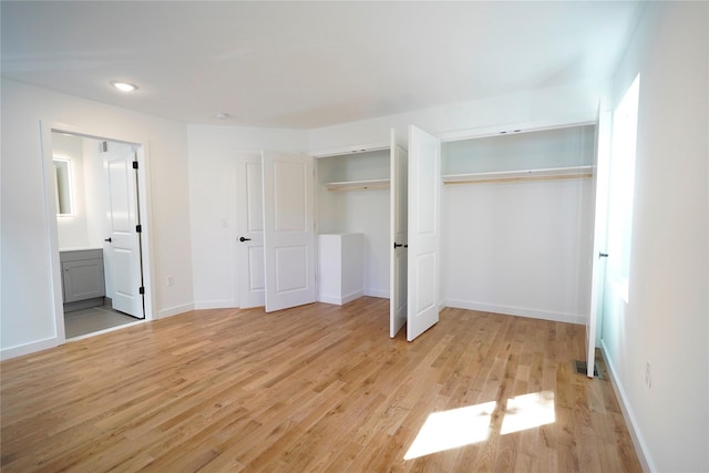 unfurnished bedroom with light wood-style floors, multiple closets, connected bathroom, and baseboards