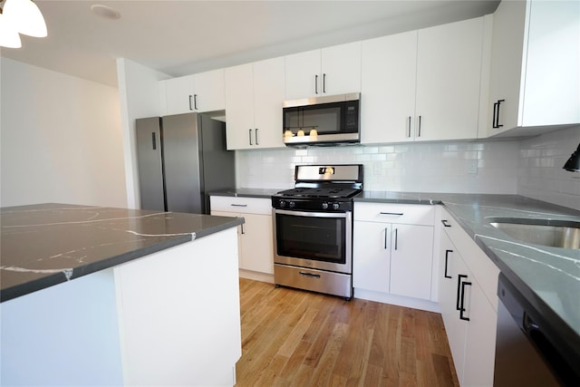 kitchen with appliances with stainless steel finishes, light wood-type flooring, tasteful backsplash, and white cabinets